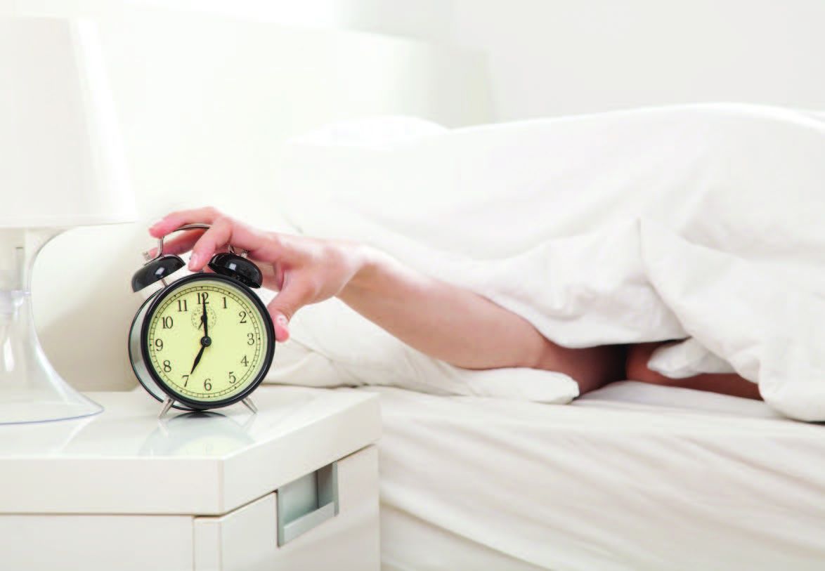 Photo d'une personne sous sa couette arrêtant son réveil pour illustrer l'article bien dormir, mieux dormir